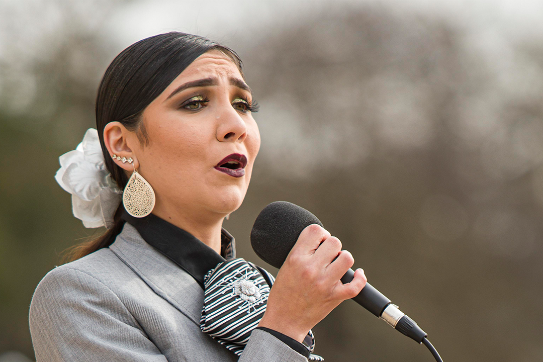 Image of female Mariachi Voces Tapatias Band singer singing with microphone in hand.